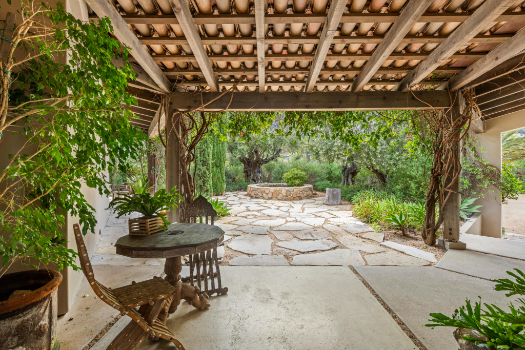 A covered patio featuring a stone path leading to a table, surrounded by greenery and outdoor decor